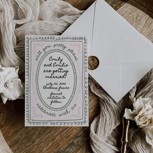 May include: A pink and green wedding invitation with a decorative border. The invitation reads "Will you pretty please... Emily and Emilio are getting married! July 25, 2025 Bordeaux, France Formal invitation to follow Celebrate with us"