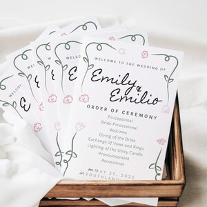 May include: A white wedding ceremony program with a floral border and the text "Welcome to the wedding of Emily & Emilio" and the order of ceremony. The date is May 25, 2025 in Southland.