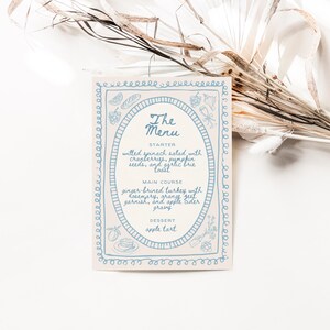 May include: A white card with a blue border and a blue oval in the center. The oval contains the text "The Menu" and lists the menu items: "Starter: Wilted spinach salad with cranberries, pumpkin seeds, and syrupy brie toast", "Main Course: Ginger brined turkey with rosemary, orange zest garnish, and apple cider gravy", "Dessert: Apple tart".