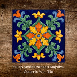May include: Square ceramic wall tile with a vibrant Italian Mediterranean Majolica design. The tile features a central floral pattern in orange, yellow, and blue, surrounded by green leaves on a deep blue background. The text "Italian Mediterranean Majolica Ceramic Wall Tile" is at the bottom.