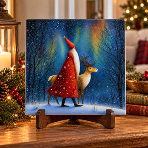 May include: A square ceramic tile featuring a painted scene of a figure in a long red cloak and pointed hat walking through a snowy forest with a reindeer. The background displays a dark blue night sky with green aurora borealis and snowfall.