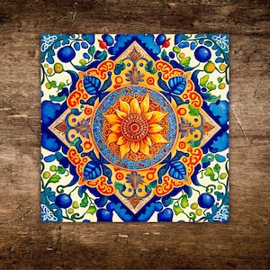 May include: Square ceramic tile with a vibrant floral design. The central motif is a yellow sunflower with orange and red accents, surrounded by a blue and gold pattern. The tile's border features blue, green, and white elements, creating a colorful, decorative piece.