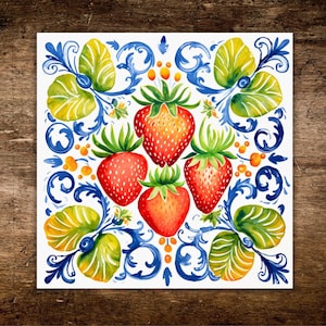 May include: A square ceramic tile featuring a central cluster of four red strawberries with green stems, surrounded by intricate blue scrollwork patterns and vibrant yellow and green leaves, set against a clean white background.