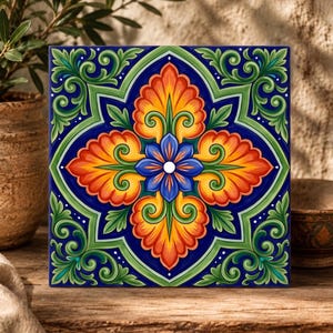 May include: A square ceramic tile featuring a symmetrical floral pattern with a central blue flower, surrounded by four orange and yellow leaf-like petals, set against a deep blue background with green scrollwork accents in the corners.
