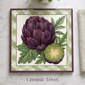 May include: Square ceramic trivet featuring a watercolor illustration of a purple artichoke and a cross-section of an artichoke with green leaves. The trivet has a green and white checkered border and a dark purple edge. The text "Ceramic Trivet" is at the bottom.