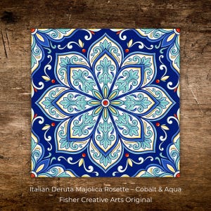 May include: Square tile with a floral rosette design in cobalt blue, aqua, yellow, and white. The tile features an intricate pattern with a central flower and surrounding scrollwork. Text at the bottom reads "Italian Deruta Majolica Rosette - Cobalt & Aqua" and "Fisher Creative Arts Original."