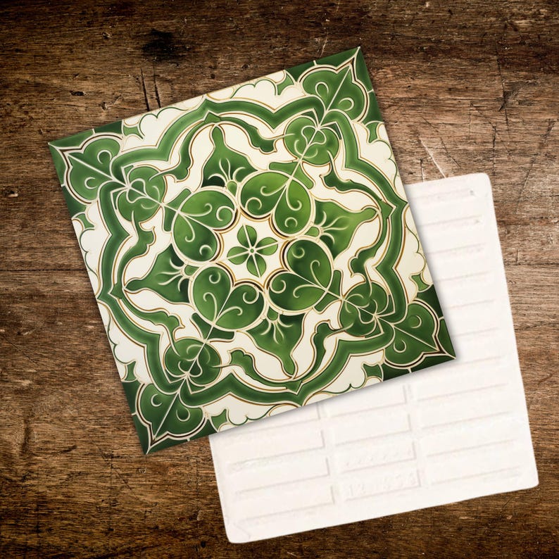 May include: Two square ceramic tiles. One tile features a green and white floral pattern with gold accents. The other tile is white with a brick pattern. The tiles are displayed on a wooden surface.