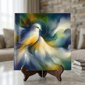 May include: A square art print featuring a watercolor painting of a white dove with yellow and blue accents. The dove is set against a backdrop of blue, green, and yellow hues. The artwork is displayed on a wooden easel.