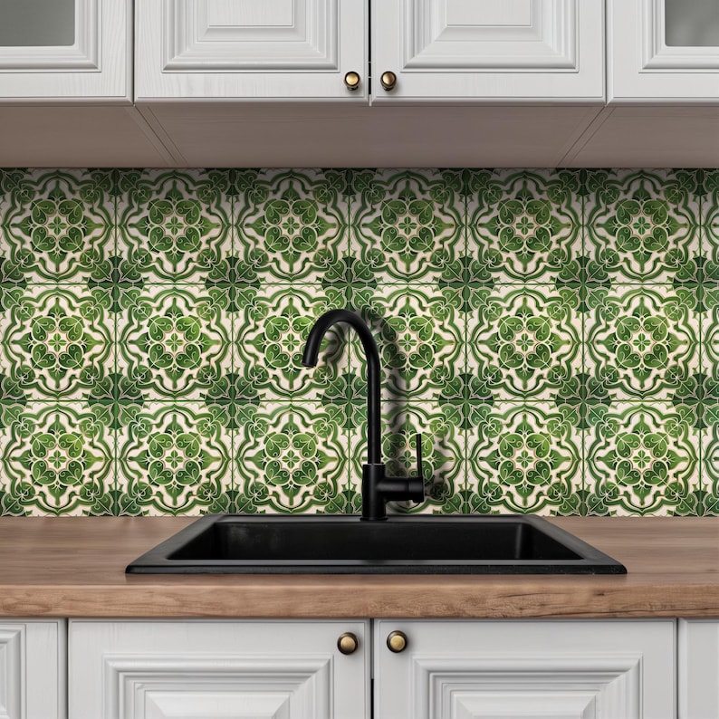 May include: A kitchen scene featuring a black sink and faucet set against a backdrop of green and white patterned tiles. White cabinets with gold knobs are visible below the countertop. The tiles have a floral design.