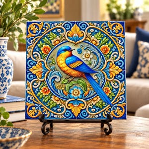 May include: A square decorative tile featuring a central blue and yellow bird perched on a branch, surrounded by intricate floral and scrollwork patterns in shades of blue, yellow, orange, and green, displayed on a black metal stand.