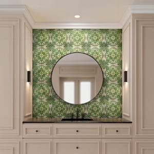 May include: A bathroom vanity with a black countertop, a round black mirror, and a green and white patterned tile backsplash. The vanity has cream-colored cabinets and two black sconces on either side of the mirror.