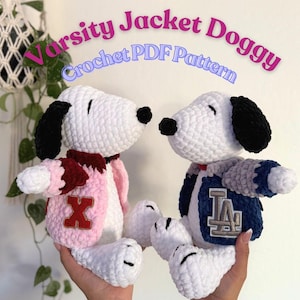 Puede incluir: Dos perros de peluche blancos tejidos a crochet que llevan chaquetas de la universidad. Un perro lleva una chaqueta rosa con una "X" roja y el otro lleva una chaqueta azul con una "LA" blanca.