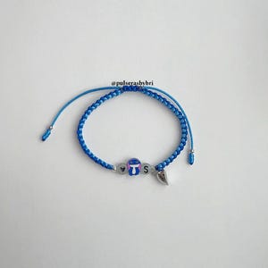 Pode incluir: Pulseira de amizade tran&ccedil;ada azul e azul claro com um pequeno amuleto Stitch, um amuleto de cora&ccedil;&atilde;o e um amuleto da letra 'S'.