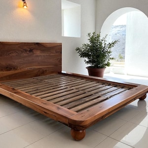 May include: A wooden bed frame with a headboard and a slatted base. The bed frame is made of a warm-toned wood and has rounded corners. The bed sits on four rounded feet. The headboard is a solid piece of wood with a natural grain.