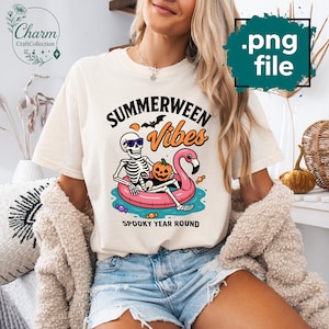 Op de afbeelding: Crèmekleurig T-shirt met de tekst "Summerween Vibes" en een afbeelding van een skelet met zonnebril, drijvend op een roze flamingo zwemband, met een pompoen. De tekst "Spooky Year Round" staat eronder.