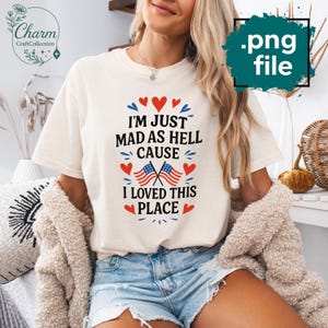 Może przedstawiać: Kremowy t-shirt z napisem "I'M JUST MAD AS HELL CAUSE I LOVED THIS PLACE" w kolorze czarnym, czerwonym i niebieskim. Projekt zawiera amerykańskie flagi i akcenty w kształcie serca. Koszulka jest połączona z dżinsowymi szortami.