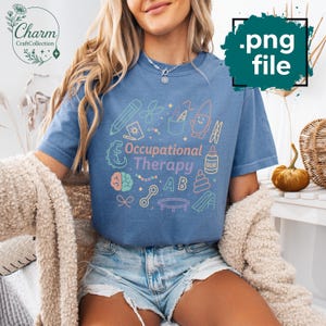 May include: A blue t-shirt with the words "Occupational Therapy" and related graphics in pastel colors. The design includes a pencil, scissors, a gnome, and other therapy-related images. The shirt is part of the Charm Craft Collection.