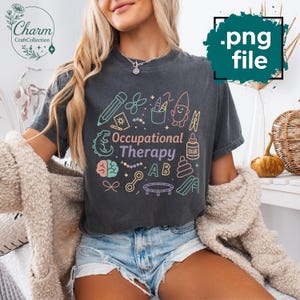 May include: Dark gray t-shirt with the words "Occupational Therapy" and related graphics in pastel colors. The design includes a pencil, scissors, crayons, a gnome, and other playful illustrations. The shirt is a .png file.
