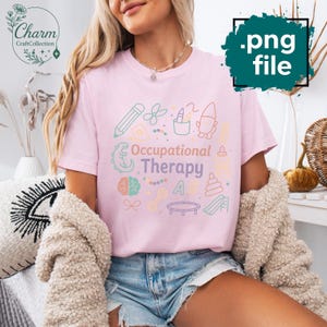 May include: A light pink t-shirt with the words "Occupational Therapy" in a colorful, playful font. The shirt features various pastel-colored illustrations related to occupational therapy, such as a pencil, scissors, and a slide.