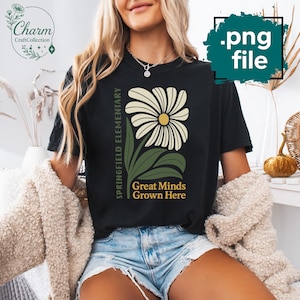May include: Black t-shirt featuring a large daisy design with a yellow center and cream-colored petals. The shirt includes the text "Springfield Elementary" and "Great Minds Grown Here" in green.