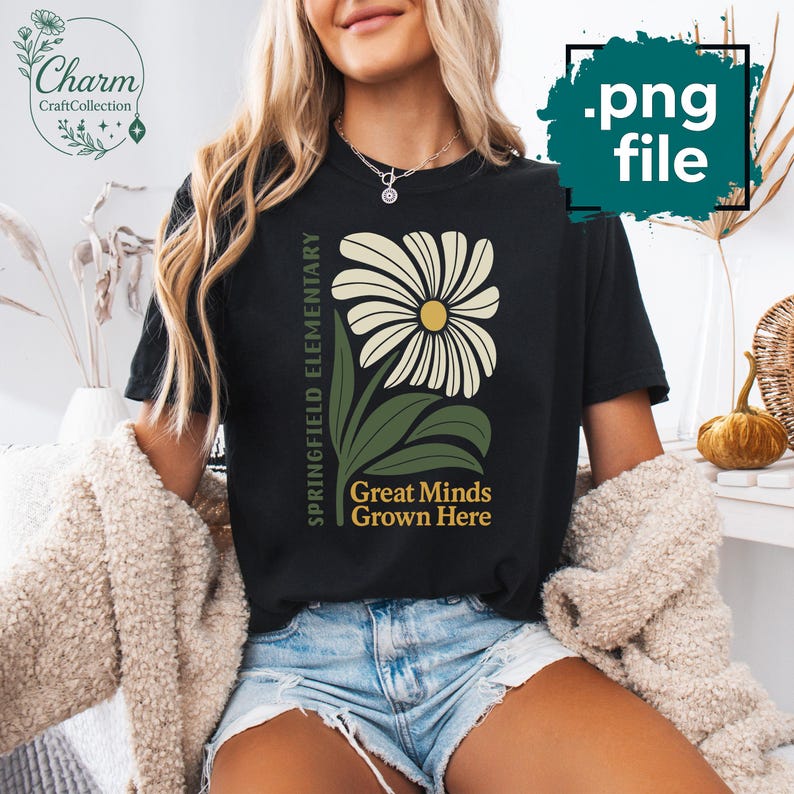 May include: Black t-shirt featuring a large daisy design with a yellow center and cream-colored petals. The shirt includes the text "Springfield Elementary" and "Great Minds Grown Here" in green.