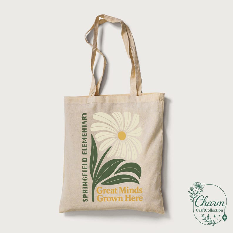 May include: Beige canvas tote bag with a floral design. The design includes a large cream-colored daisy with a yellow center, green leaves, and the text "SPRINGFIELD ELEMENTARY" and "Great Minds Grown Here" in green and gold.