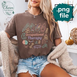 May include: Brown t-shirt with the words "Occupational Therapy" and colorful illustrations of school supplies and toys. The shirt has a crew neck and short sleeves. The design includes a pencil, scissors, and a brain.