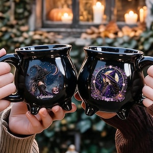 May include: Two black ceramic cauldron-shaped mugs with three small feet and handles. The left mug features a witch illustration and the name Aurelia. The right mug displays a witch in a purple circle with the name Fiora and pumpkin accents.