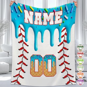 May include: A white baseball-themed blanket with a blue, dripping icing design at the top, sprinkled with colorful candies. The word "NAME" is in white block letters. The number "00" is in a waffle cone design.