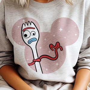 May include: A gray sweatshirt with a pink Mickey Mouse ear design featuring a cartoon image of Forky from Toy Story. Forky is wearing a red ribbon and has a blue face with a single eye.