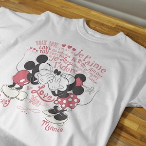 May include: White t-shirt with a graphic of Mickey Mouse and Minnie Mouse kissing. The shirt has the text "True Love" and "Je t'aime" in pink lettering.