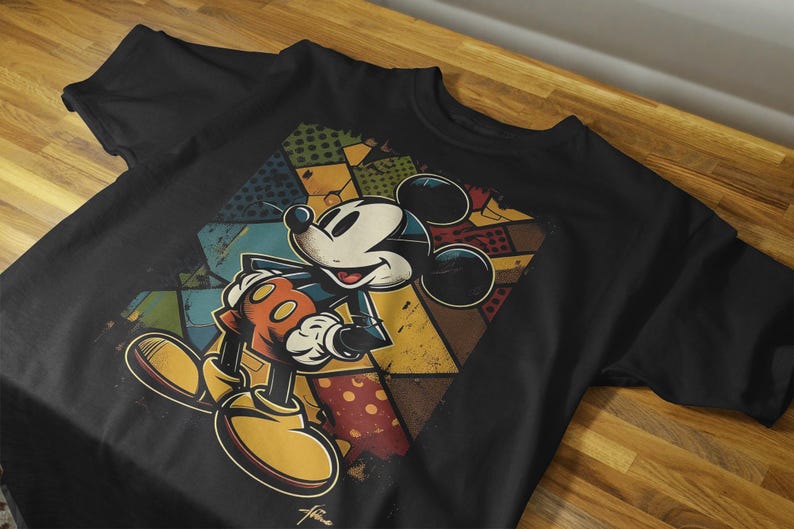 May include: Black t-shirt with a colorful graphic of Mickey Mouse in a retro style. The graphic features Mickey Mouse standing with his arms crossed and a colorful geometric pattern behind him.