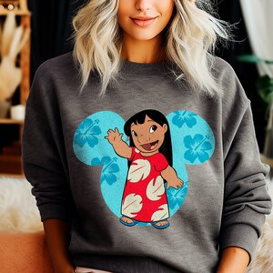 May include: A gray sweatshirt with a blue Mickey Mouse ear design featuring a cartoon character of Lilo from the Disney movie Lilo & Stitch. The character is wearing a red dress with white flowers and is waving.