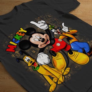 K&ouml;nnte beinhalten: Ein schwarzes T-Shirt mit einer bunten Grafik von Mickey Mouse, Pluto und Goofy. Der Text "Mickey" ist in Regenbogenfarben auf dem Shirt gedruckt.