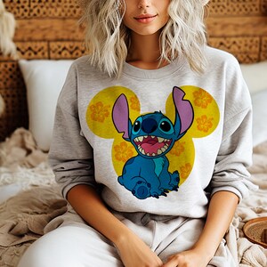 May include: Gray sweatshirt with a blue Stitch character wearing a yellow Mickey Mouse ear design with orange hibiscus flowers.