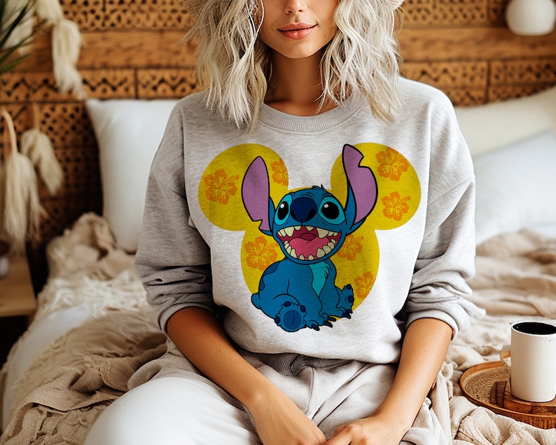 May include: Gray sweatshirt with a blue Stitch character wearing a yellow Mickey Mouse ear design with orange hibiscus flowers.