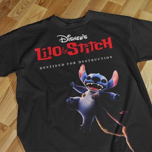 May include: Black t-shirt featuring the Disney's Lilo & Stitch logo in red and white. The shirt has a graphic of Stitch, a blue alien, with his mouth open. The text "DESTINED FOR DESTRUCTION" is below the logo.
