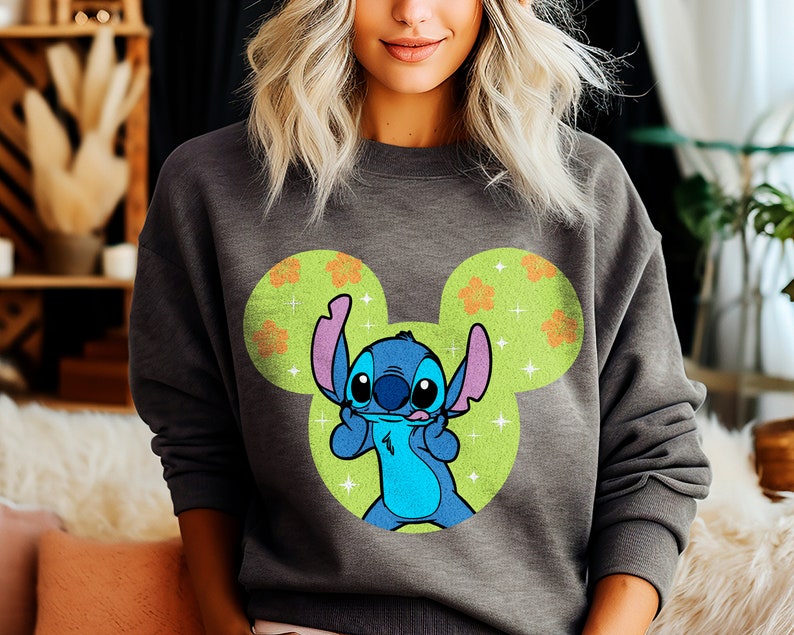 May include: Gray sweatshirt with a blue Stitch character wearing a Mickey Mouse ear hat. The hat is green with orange flowers and white sparkles.