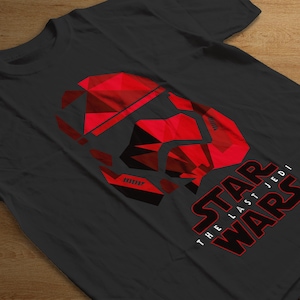 Puede incluir: Camiseta negra con un diseño geométrico de casco de Stormtrooper en rojo y negro. El texto "STAR WARS THE LAST JEDI" está impreso en rojo y blanco debajo.