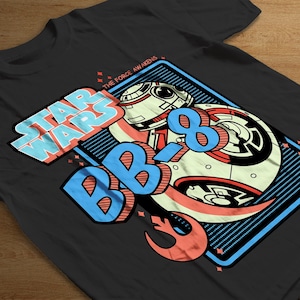 Puede incluir: Camiseta negra con un gráfico colorido del personaje BB-8 de Star Wars. El diseño incluye las palabras "STAR WARS" y "BB-8" en una fuente estilizada, junto con la frase "THE FORCE AWAKENS".