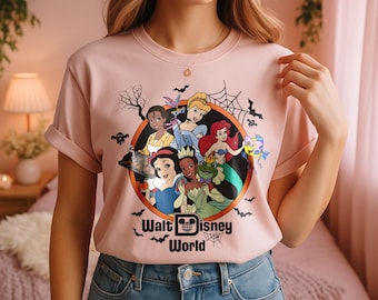 May include: A light pink t-shirt featuring a graphic of Disney princesses in a Halloween-themed design. The design includes bats, spiderwebs, and the words "Walt Disney World". The shirt is made of a soft material.