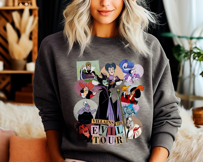 Puede incluir: Sudadera gris oscuro con un gr&aacute;fico colorido de villanos de Disney en marcos circulares. El gr&aacute;fico incluye personajes como Mal&eacute;fica y &Uacute;rsula, con el texto "Villains The Evil Tour" debajo. La sudadera est&aacute; hecha de un material suave.