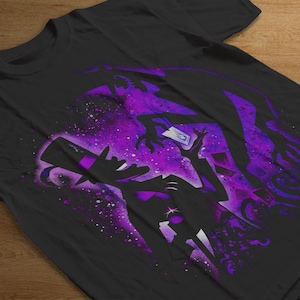 Puede incluir: Camiseta negra con un dise&ntilde;o gr&aacute;fico morado y blanco. El dise&ntilde;o representa la silueta de un mago sosteniendo una carta, con un fondo c&oacute;smico y una figura sombr&iacute;a. La camiseta est&aacute; hecha de un material suave.