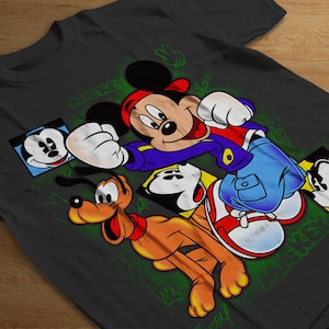 May include: A black t-shirt with a colorful graphic print of Mickey Mouse, Pluto, and other Disney characters. The graphic features the characters in a cartoon style with bright colors and bold outlines. The text "Mickey Mouse" is printed on the shirt in a green font.