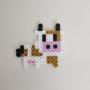 May include: A brown, white, and black cow made of small plastic beads. The cow has a pink nose and black eyes.