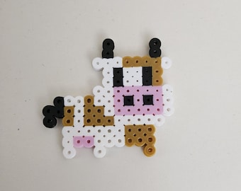 May include: A brown, white, and black cow made of small plastic beads. The cow has a pink nose and black eyes.