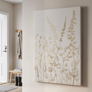Pode incluir: Arte de parede em tela com um design botânico. A obra apresenta ilustrações florais douradas sobre um fundo neutro esbranquiçado. O design inclui representações detalhadas de caules e folhas de plantas, criando uma estética natural.