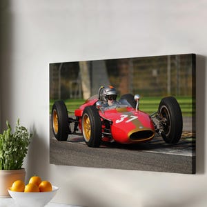 May include: A red vintage race car with the number 37 on the side, driven by a person wearing a helmet, on a race track.