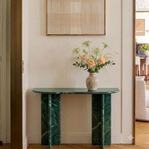 May include: A semi-circular green marble console table with a smooth top and two vertical slab legs. A speckled ceramic vase sits on the table, holding a bouquet of light orange ranunculus flowers and green foliage.