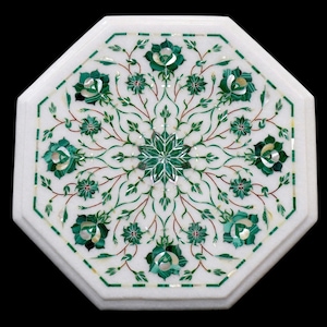 May include: White octagonal marble table with a detailed floral inlay design. The intricate pattern features green and white floral elements, with a central starburst design. The table's edges are also decorated with a green and white border.